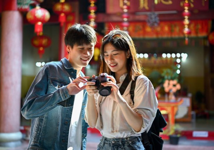 Happy and smiling young Asian tourist couple enjoying their old town sightseeing, taking photos and visiting a Chinese temple together.