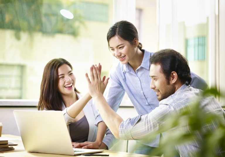young asian business person giving coworker high five in office celebrating achievement and success.